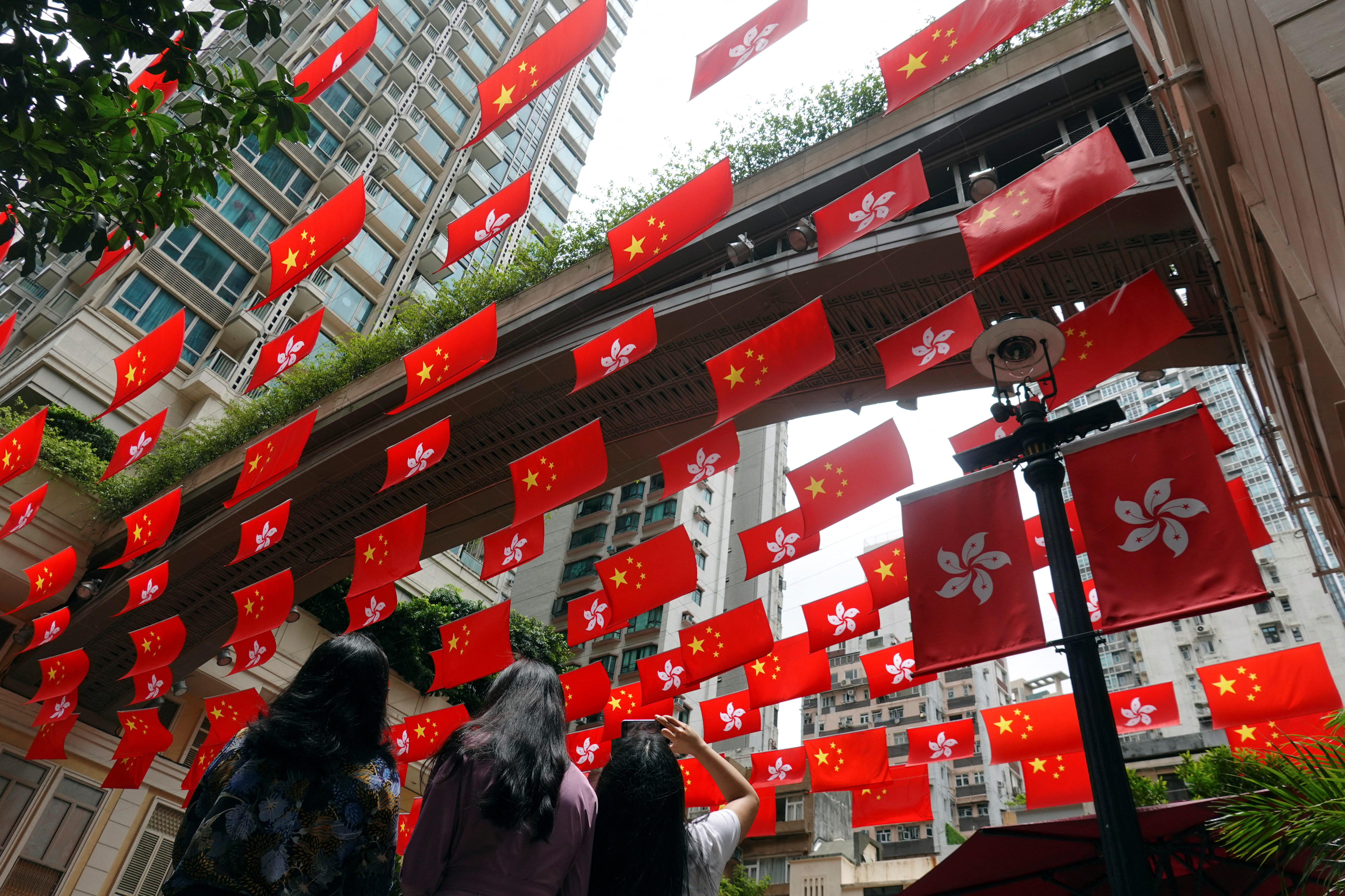 A woman takes pictures of Chinese and Hong Kong flags decorating a street, ahead of the 25th anniversary of the handover of the former British colony to Chinese rule, in Hong Kong, China, June 30, 2022 (Reuters/Joyce Chu)